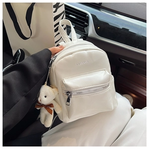 Primer plano de mini mochila blanca con cremallera plateada y amuleto de oso de peluche