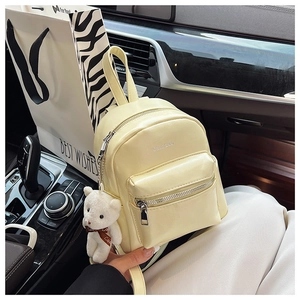 Detalle de mini mochila amarillo crema con colgante de oso de peluche y bolsillo frontal