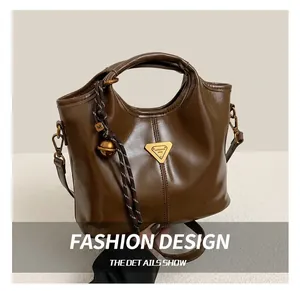 Detail of dark brown leather tote bag featuring a gold metal badge and braided charm