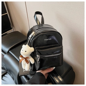 Detalle de mini mochila negra brillante con letras impresas y colgante de oso blanco