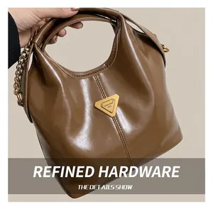 Macro shot of glossy brown leather handbag featuring a golden triangle metal logo plaque