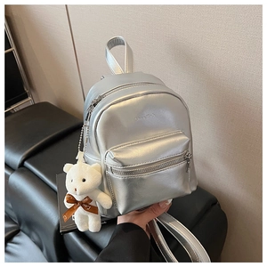 Detalle de una mini mochila plateada con acabado metálico y llavero de oso peluche
