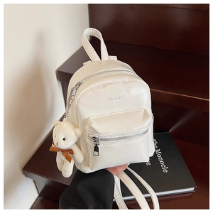 Primer plano de mini mochila crema con llavero de oso sobre fondo de madera oscura