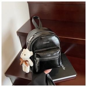 Detalle de mini mochila de charol negro brillante con colgante de oso de peluche