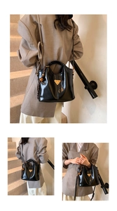 Detail of glossy black tote bag featuring a metallic triangle logo and woven strap accents