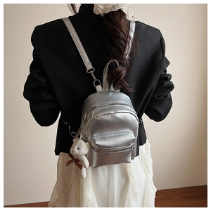 Detalle de mini mochila plateada metalizada con un tierno colgante de oso de peluche