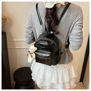 Vista trasera de una mini mochila negra brillante para mujer con colgante de osito de peluche