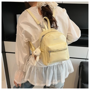 Detalle de mini mochila amarillo pálido brillante con oso de peluche y textura de cuero