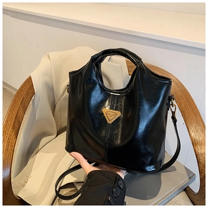 Detail of black glossy tote bag with golden triangular metal logo on a wooden chair
