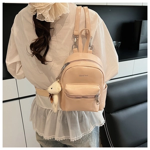 Detalle de mini mochila de cuero PU rosa claro con un lindo peluche de oso blanco colgado