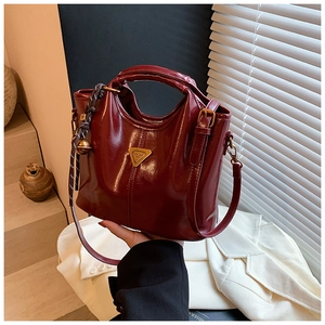 Detail of reddish brown glossy leather handbag with golden hardware and bell charm