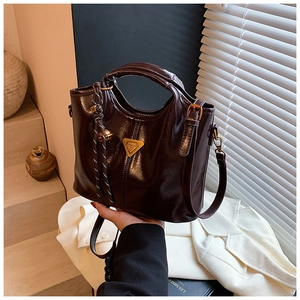 Detail view of brown faux leather handbag featuring a gold hardware logo and braided charm