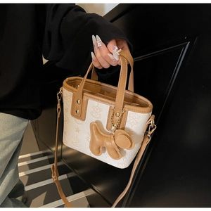 Detail of a mini beige tote bag with brown trim and cute dog charm handheld by a model