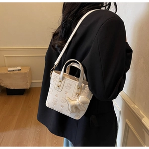 Detail of white embossed leather tote bag with star logo and cute bear charm accessory