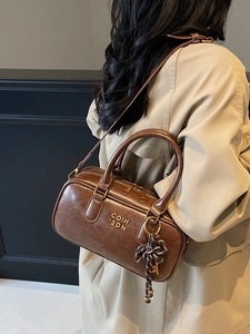 Retro brown Boston handbag with gold hardware and decorative charm on tan trench coat