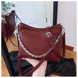 Detail of burgundy leather bucket bag with silver geometric chain and adjustable strap