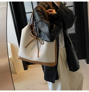 Detail of large tote bag in white fabric and brown leather trim with woven bow detail