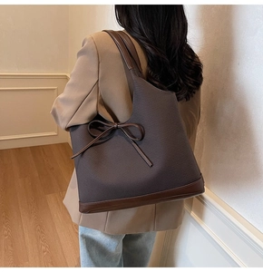 Detail of dark brown tote bag with ribbon bow and leather trim worn by model
