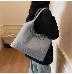 Detail of light blue tote bag with woven texture and decorative bow on a model shoulder