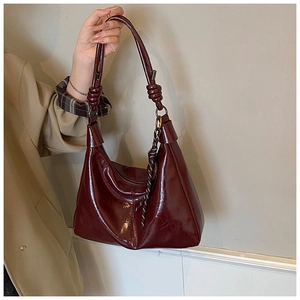 Détail d'un sac hobo rouge foncé brillant avec nœud tressé unique sur la bandoulière