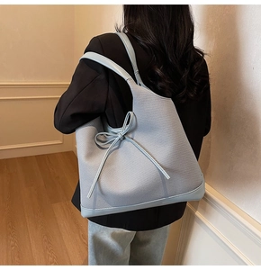 Detail view of woven large tote bag with contrast leather trim and side bow on model