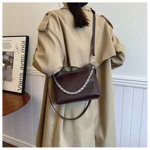 Close-up of deep brown leather bucket bag with silver chain on model in beige coat