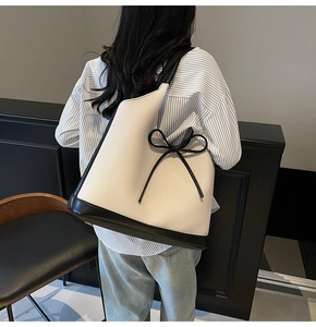 Detail of the large beige woven tote bag featuring black leather trim and a chic bow detail