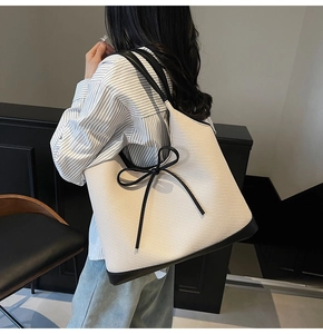Detail of minimalist tote bag with contrast black trim and delicate leather bow accent