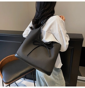 Detail of woven texture contrast with smooth leather and a thin bow on a black tote bag