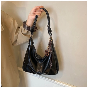 Détail du sac hobo en cuir verni noir brillant avec bandoulière nouée et pendentif