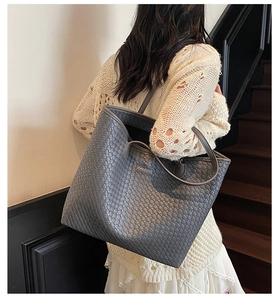 Close-up of dark grey woven tote bag featuring a textured pattern and metallic logo detail