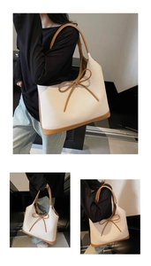 Detail of a large cream woven tote bag with brown leather handles and a bow detail