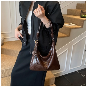 Détail du sac à bandoulière en cuir verni marron foncé avec poignée décorative à nœud