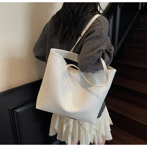 White woven leather tote bag shown on model's shoulder in a stylish indoor setting