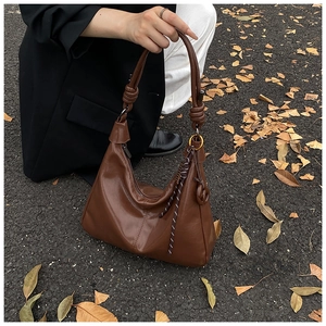 Détail du sac hobo marron brillant avec poignée nouée et surpiqûres verticales