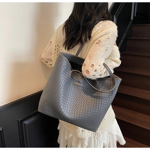 Detail of grey woven tote bag featuring metal logo plate and slim shoulder straps