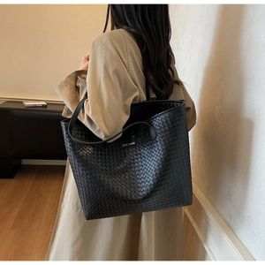 Detail of black woven tote bag with leather straps and ZINE PARIS label on a beige coat