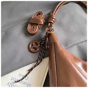 Détails d'un sac cabas en cuir verni marron avec anneaux métalliques et pendentif tressé