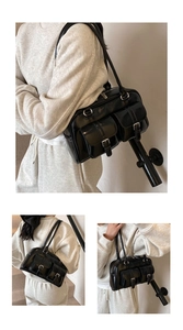 Detail of a large black faux leather shoulder bag with front buckle pockets and long straps