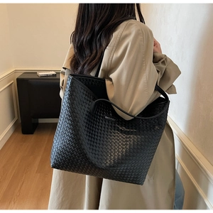 Detail shot of the black woven leather texture and shoulder strap on the large tote bag