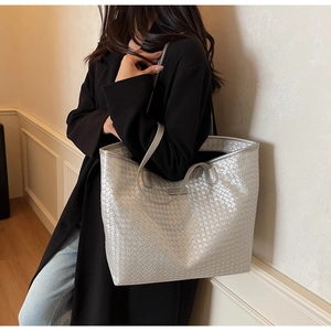 Detail of silver woven tote bag featuring metallic texture and slim top handles