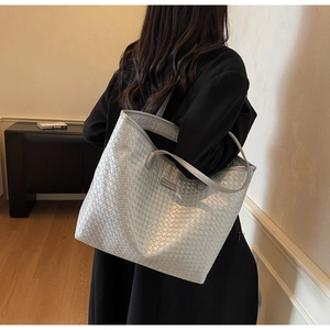 Detailed view of silver woven leather tote bag with metallic logo on textured surface