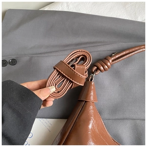 Détail d'un sac cabas marron brillant montrant l'attache de la bandoulière et les coutures