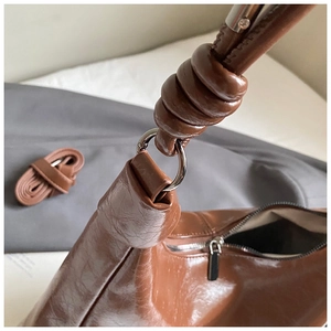 Détail d'un sac bandoulière marron en similicuir avec bandoulière nouée et anneau métal