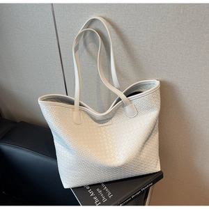 Detail of white woven leather tote bag featuring a square logo patch on a leather sofa
