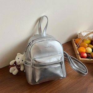 Mini mochila plateada metalizada con colgante de oso blanco en mesa de madera oscura