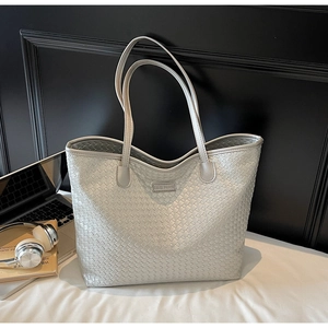 Detail of silver woven tote bag featuring a branded label and fine handle textures
