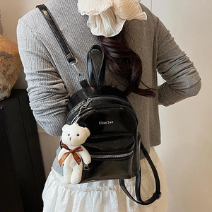 Mochila pequeña elegante de charol negro con colgante de oso en un atuendo casual