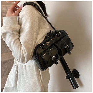 Detail of a black glossy shoulder bag with vintage buckles worn over a cream sweatshirt