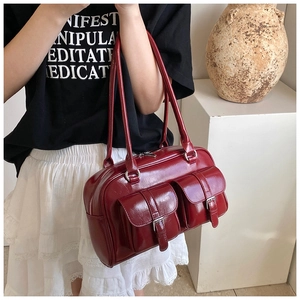 Close-up of glossy wine red Boston bag showing front buckle pockets and smooth leather texture